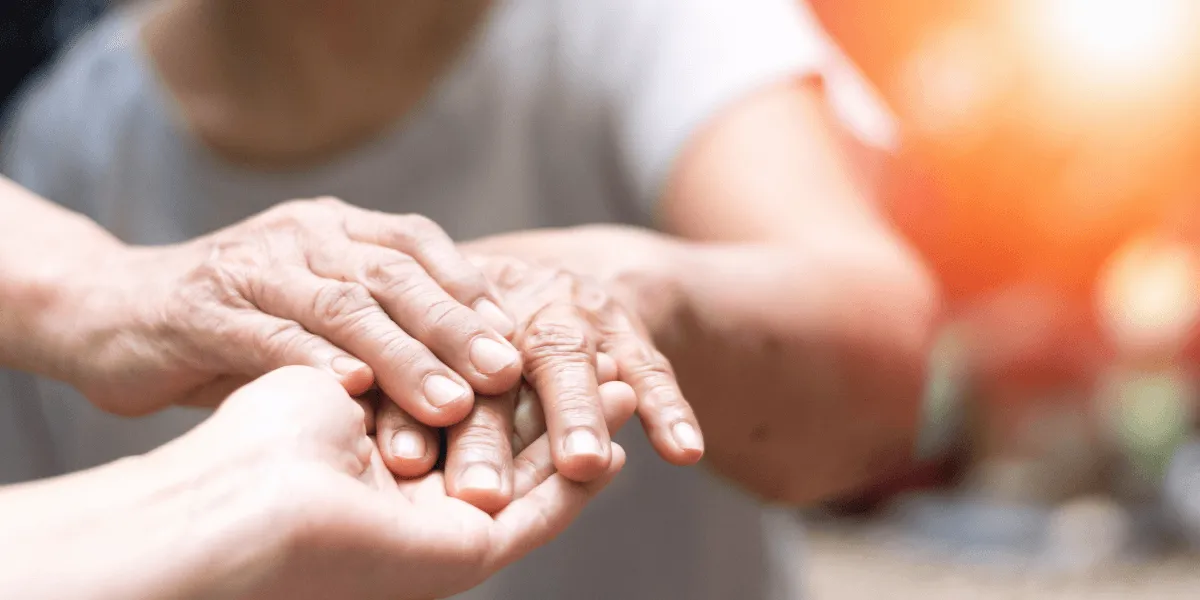 Berufskrankheit Parkinson: Eine Person hält behutsam die Hände eines älteren Menschen als Zeichen von Unterstützung und Fürsorge.