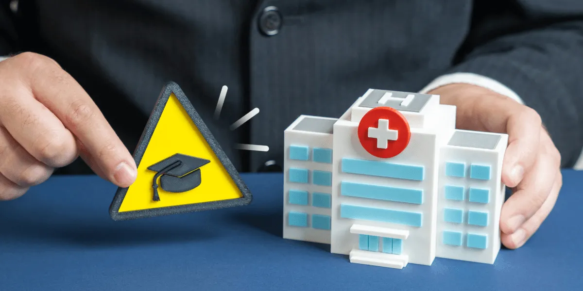 KHAG: Geschäftsmann hält ein Modell eines Krankenhauses neben ein gelbes Warnschild mit Doktorhut als Symbol für Risiken oder Herausforderungen im Gesundheits- und Bildungsbereich.