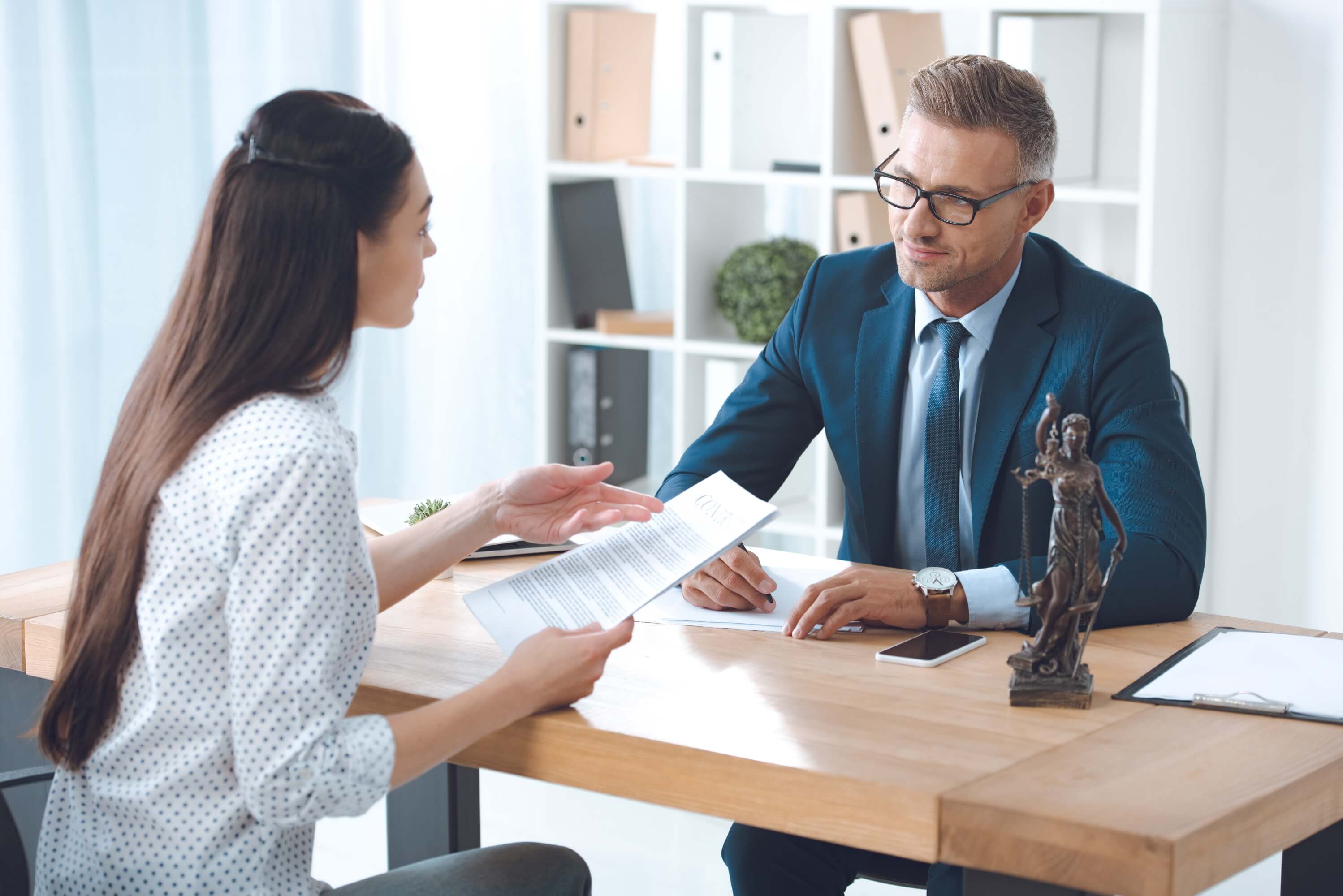 Eine Frau und ein Mann in Business-Kleidung besprechen Unterlagen an einem Tisch mit Iustitia-Figur