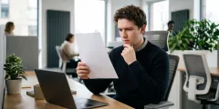 Auszubildender sitzt grübelnd im Büro vor der ausgedruckten Kündigung seines Ausbildungsvertrags