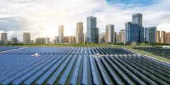 Energy Sharing: Solaranlage mit langen Reihen von Photovoltaikmodulen vor einer modernen Stadtsilhouette bei Sonnenlicht.