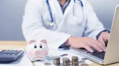 GKV-Spargesetz: Arzt arbeitet am Laptop; im Vordergrund stehen ein Sparschwein, gestapelte Münzen, ein Taschenrechner und Unterlagen mit Diagrammen auf dem Schreibtisch.