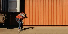 Arbeiter in Warnweste schützt sich auf einem sonnigen Betriebsgelände vor starker Hitze.