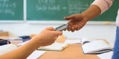 Nahaufnahme der Hand einer Schülerin, die ihrer Lehrerin ihr Handy übergibt wegen des Handyverbots an Schulen